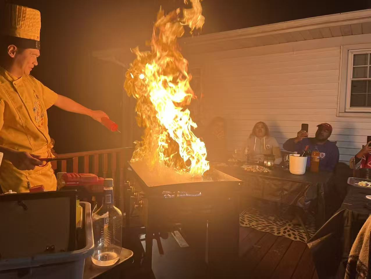Hibachi chef performing a dramatic fire show on the grill while guests watch and record