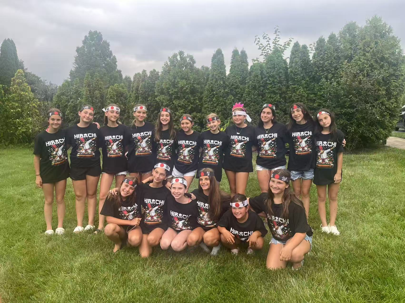 Group of kids wearing matching Hibachi t-shirts and Japanese headbands posing together on a lawn