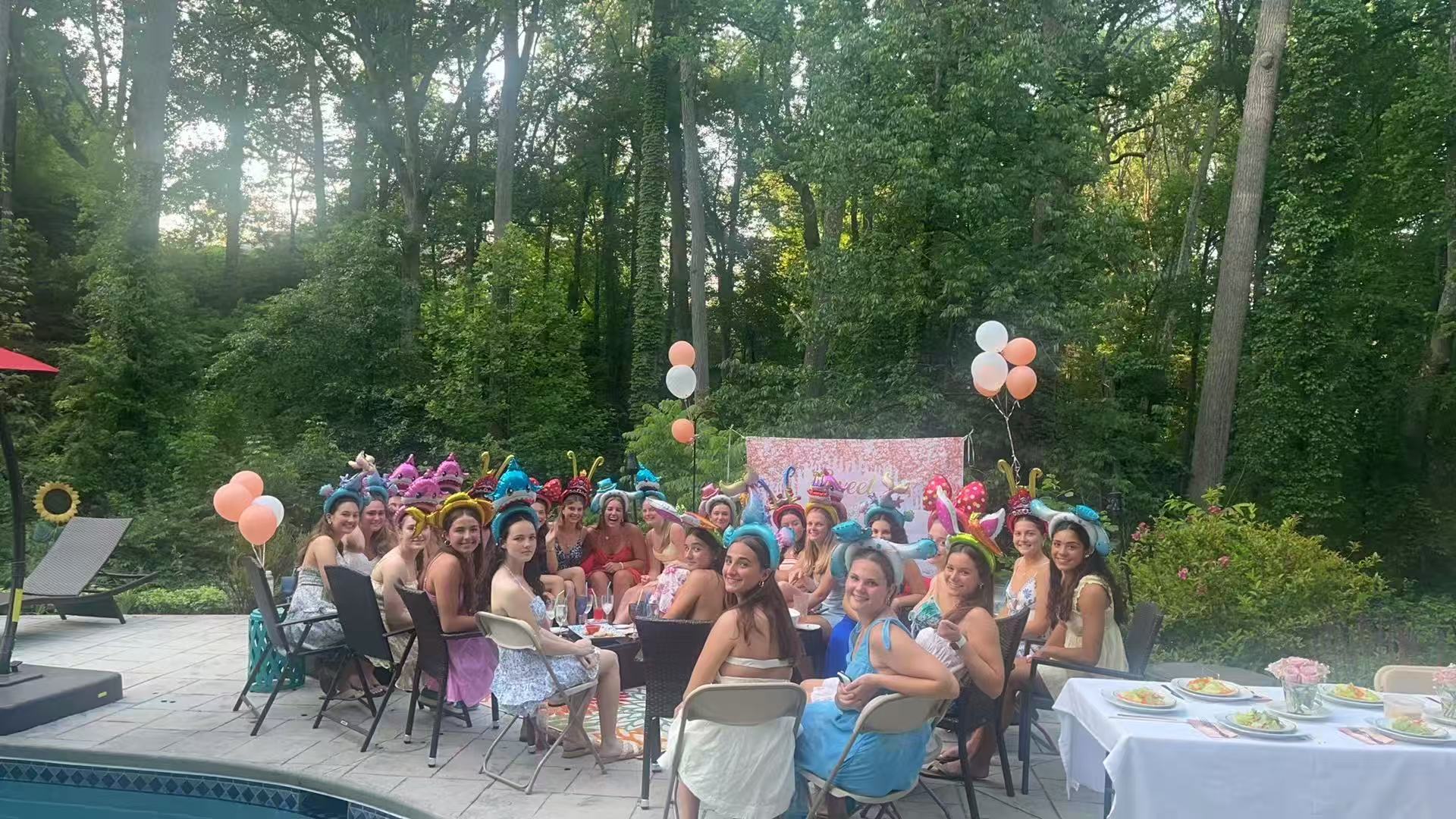 Large poolside party with women wearing colorful headbands and balloons in the background